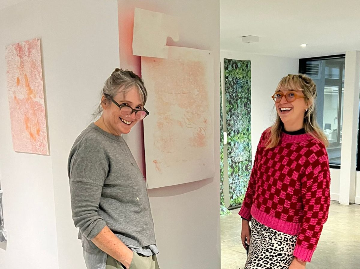 two women standing in front of a piece of art laughing